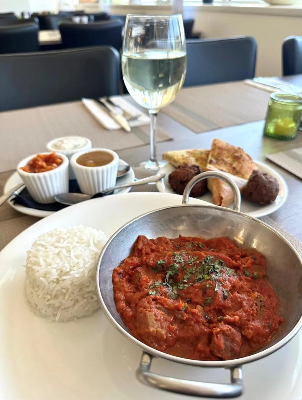 A curry with rice and sides, with a glass of white wine
